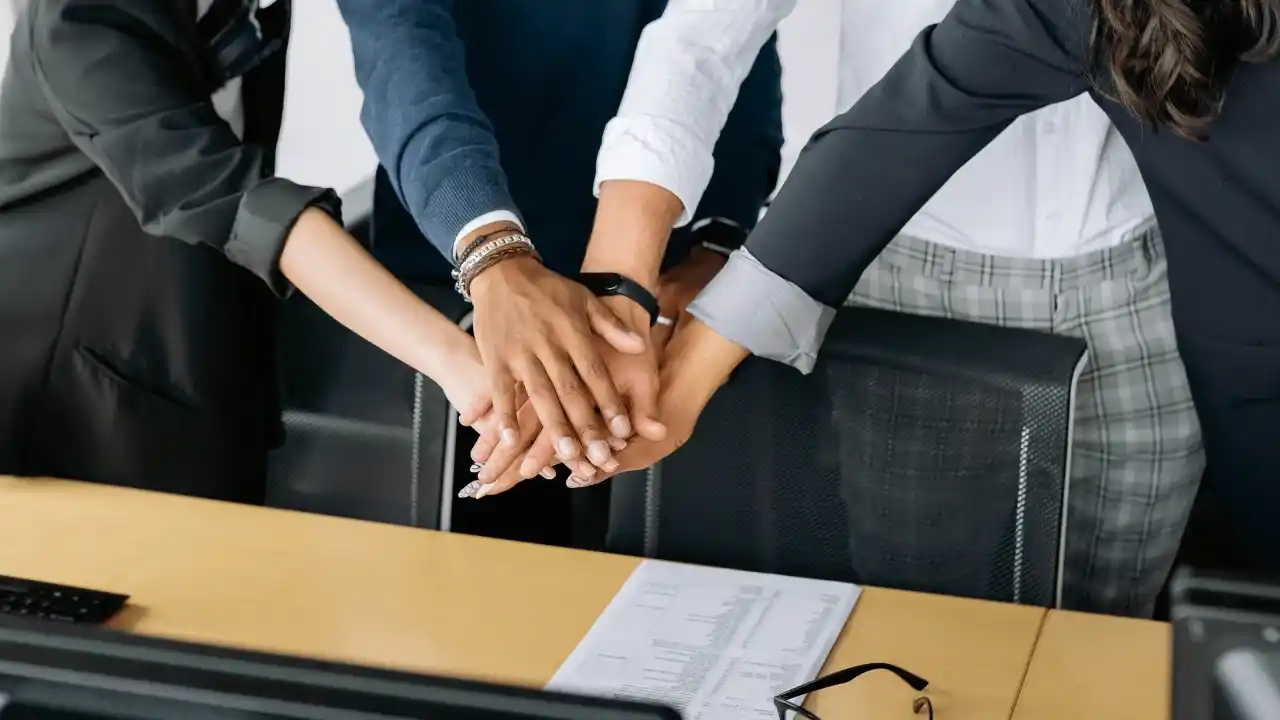 Equipo de trabajo uniendo las manos sobre una mesa, simbolizando colaboración y compromiso profesional.
